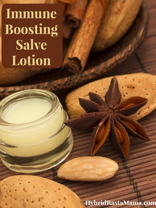 Immune boosting lotion in a small glass lip gloss type jar. Dried cloves, cinnamon, and other herbs surround it on a bamboo mat. 