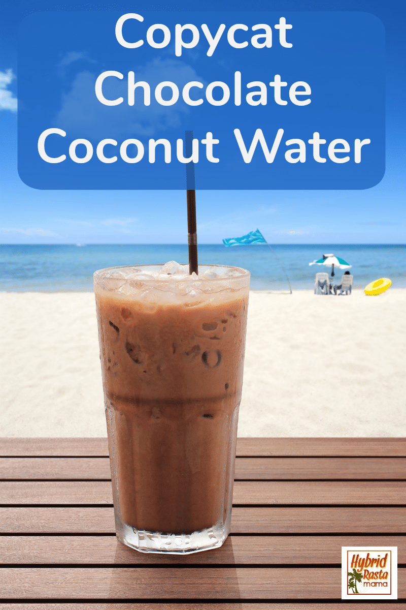 A glass of copycat chocolate coconut water on a white sand beach