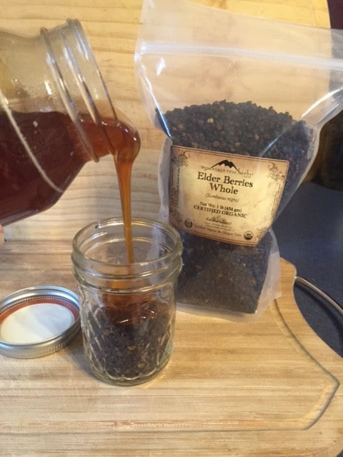 Pouring honey over dried elderberries in mason jar for elderberry elixir